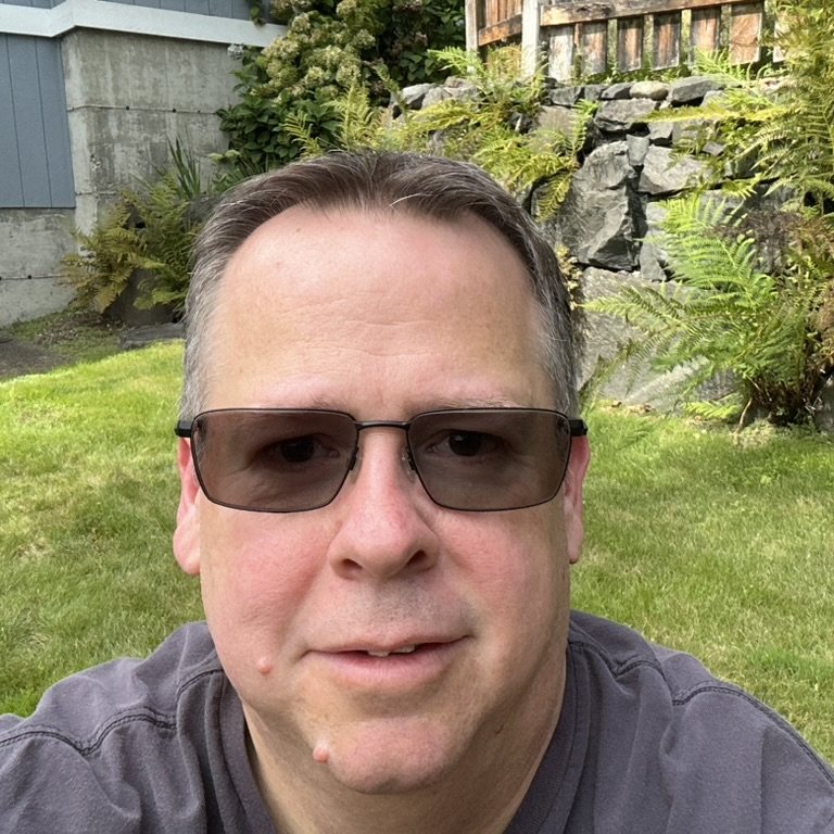 Andy Duckworth outdoors on a lawn with ferns and a stone wall behind him